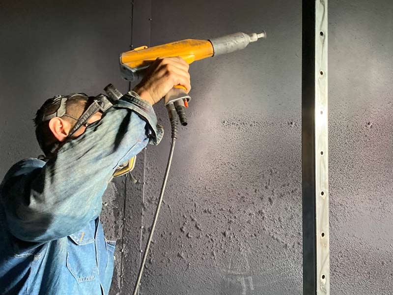 Operador de Home Athletic realizando pintura electrostática a piezas de metal durante proceso de Fabricación de Máquinas para Gimnasio